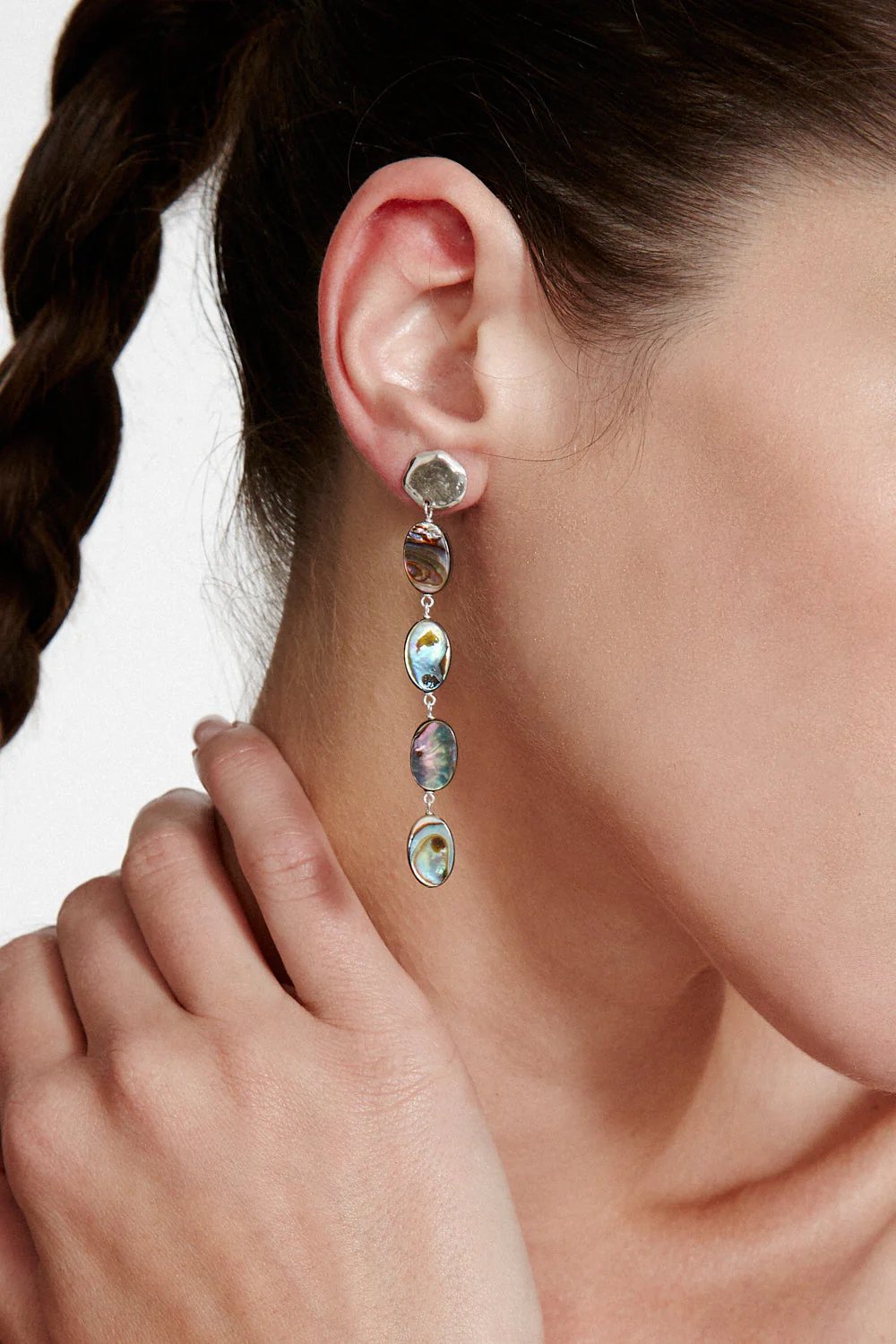 Close-up of a woman wearing a dangling earring with iridescent abalone.