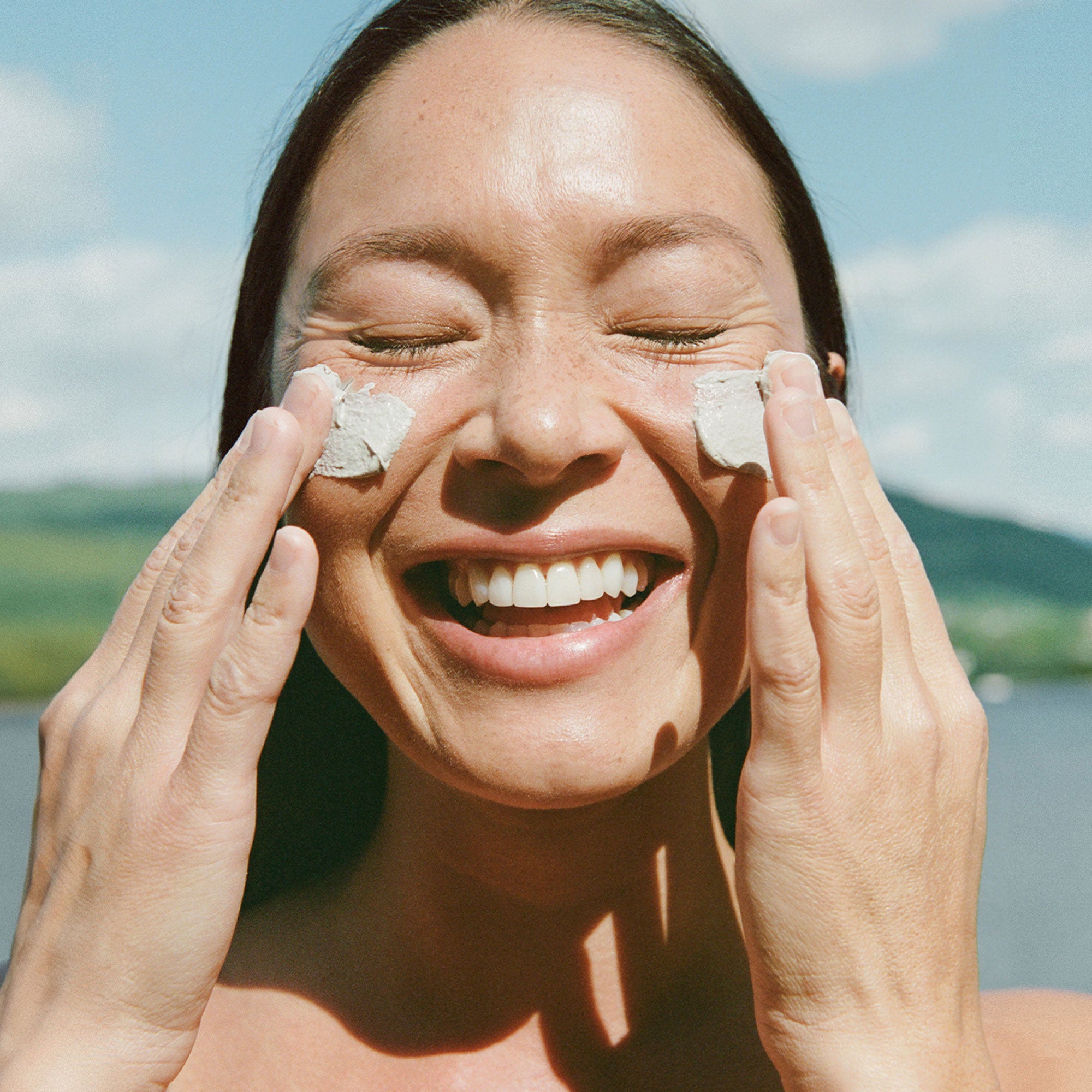 Woman applying cream to her face with a scenic background