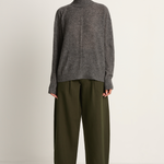 Person wearing a gray turtleneck sweater and olive green pants on a plain background