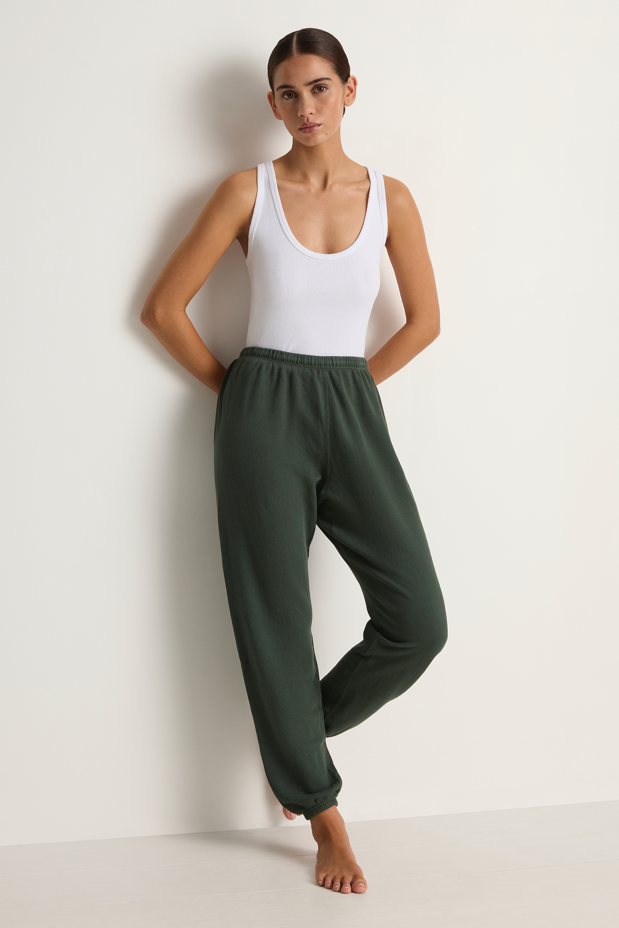 Woman wearing a white tank top and green pants against a plain background