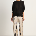 Woman wearing a black sweater and patterned pants on a white background