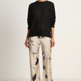 Woman wearing a black sweater and patterned pants on a white background
