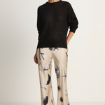 Woman wearing a black sweater and patterned pants on a white background
