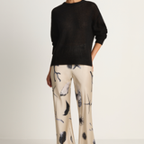 Woman wearing a black sweater and patterned pants on a white background