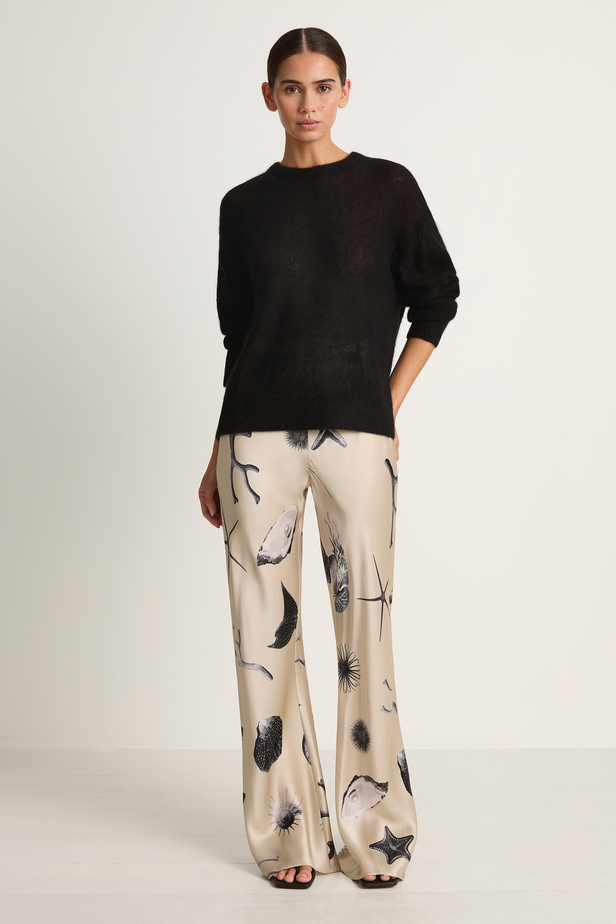 Woman wearing a black sweater and patterned pants on a white background