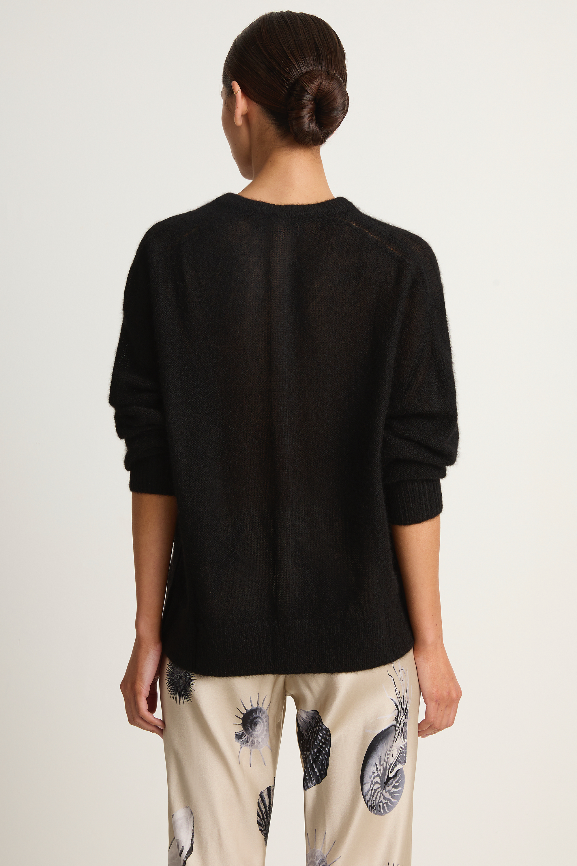 Person wearing a black sweater with patterned pants on a white background