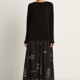 Woman wearing a black long-sleeve top and black skirt with animal concert print on a white background