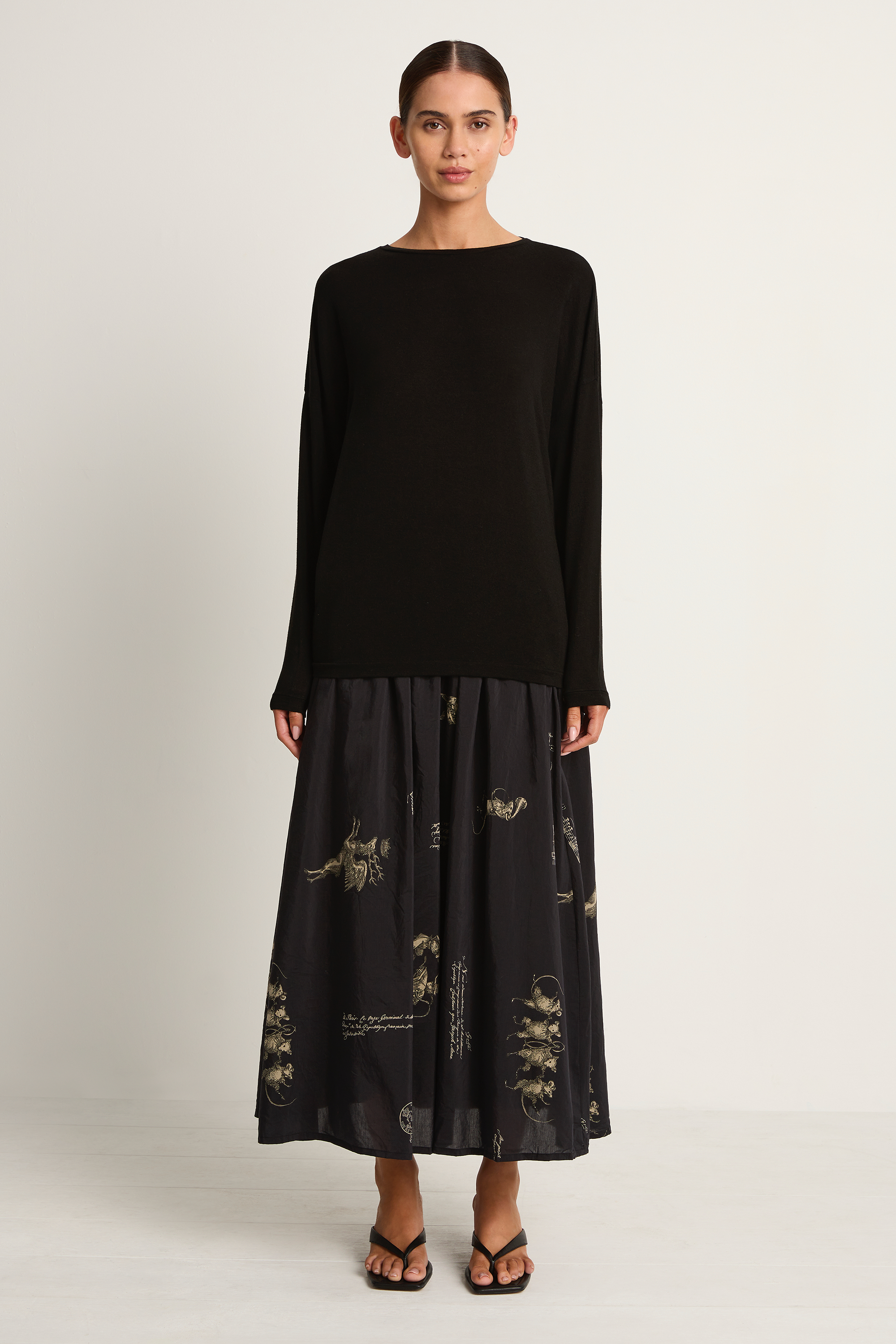 Woman wearing a black long-sleeve top and black skirt with animal concert print on a white background