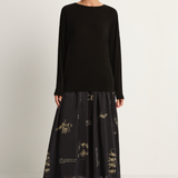 Woman wearing a black long-sleeve top and black skirt with animal concert print on a white background