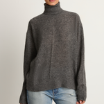 Woman wearing a gray turtleneck sweater and light blue jeans on a plain background