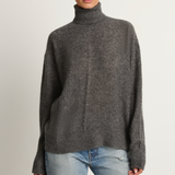 Woman wearing a gray turtleneck sweater and light blue jeans on a plain background