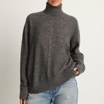 Person wearing a gray turtleneck sweater and light blue jeans on a plain background