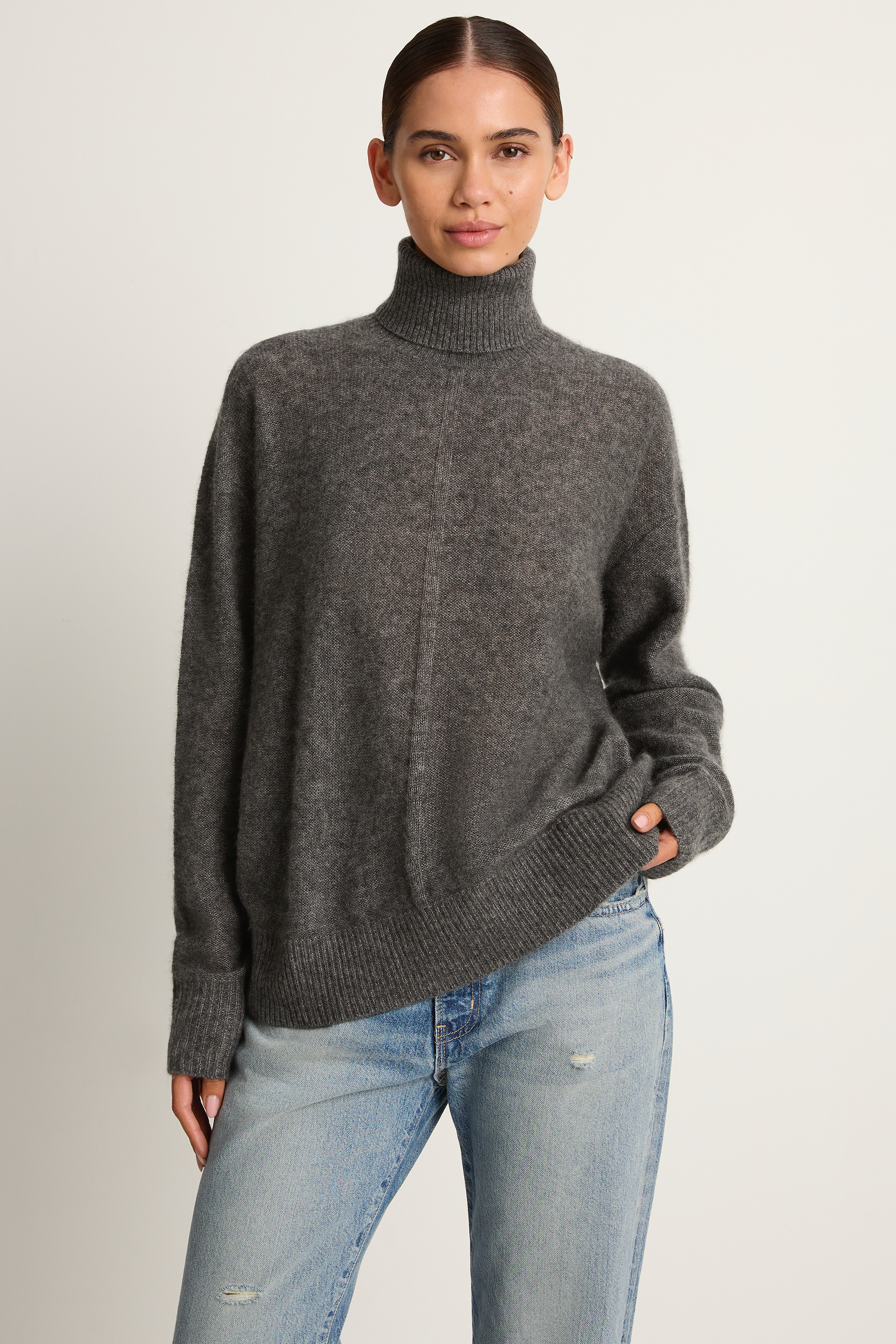 Person wearing a gray turtleneck sweater and light blue jeans on a plain background