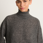 Woman wearing a gray turtleneck sweater against a plain background