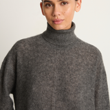 Woman wearing a gray turtleneck sweater against a plain background