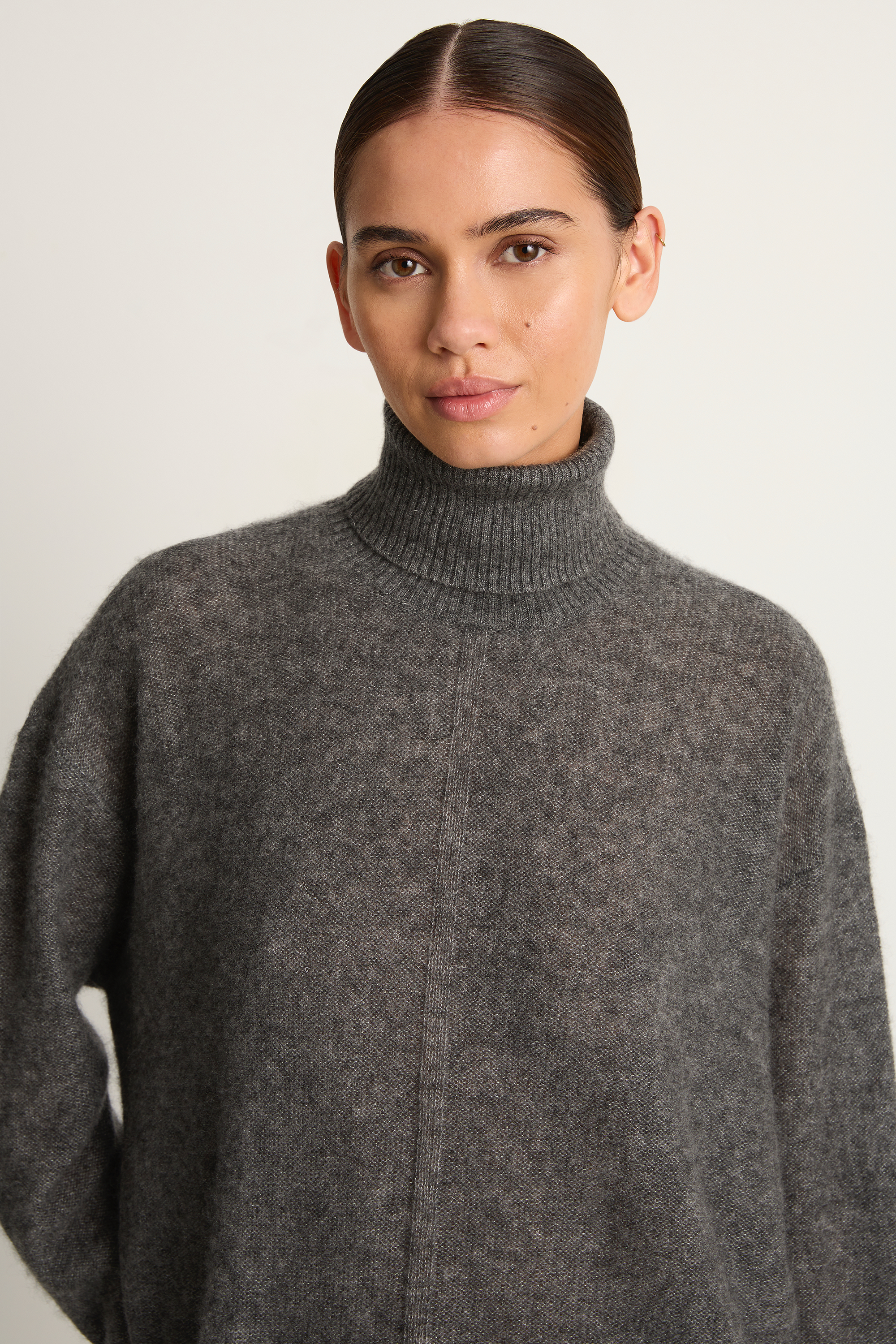 Woman wearing a gray turtleneck sweater against a plain background