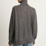 Person wearing a gray sweater and blue jeans on a plain background