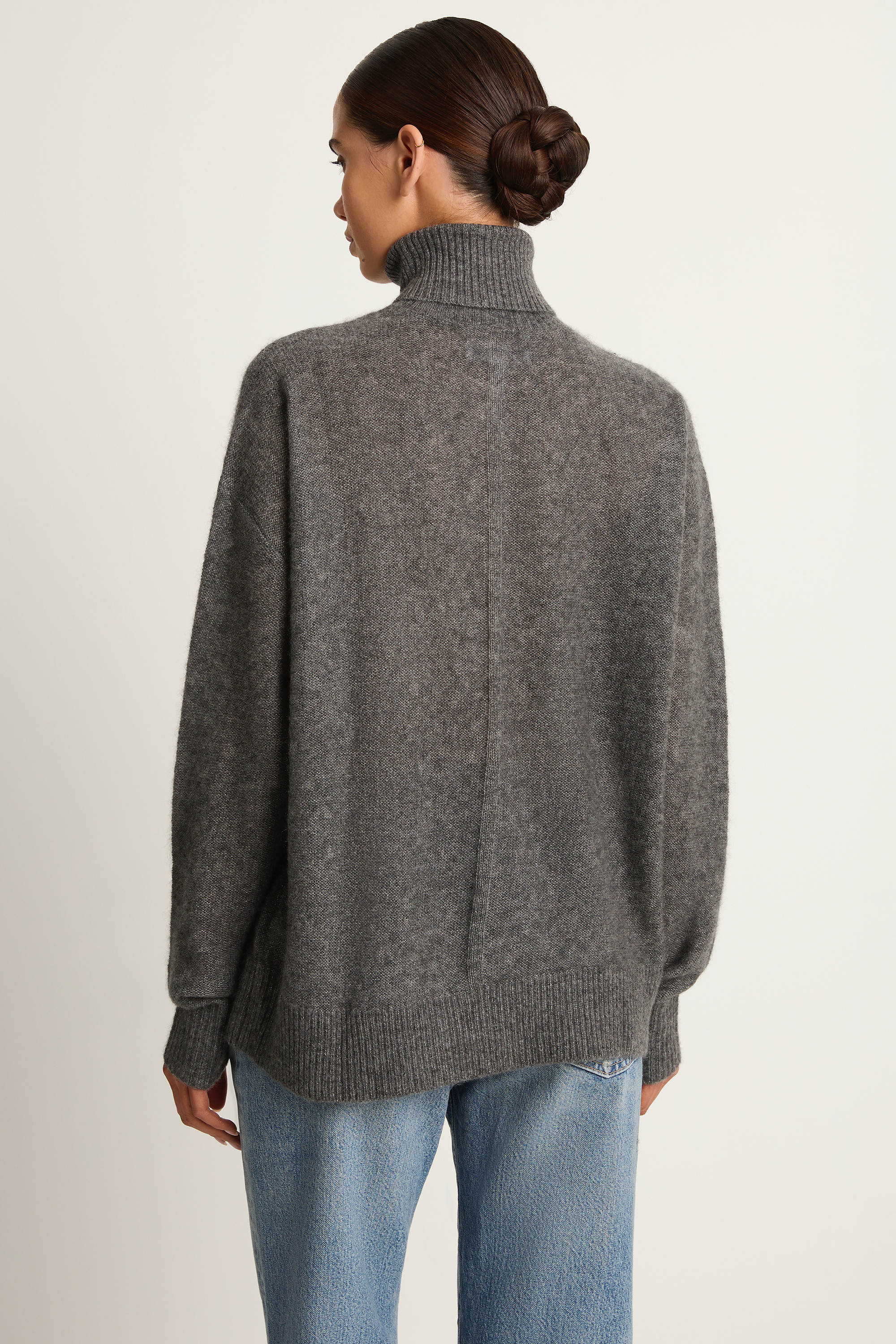 Person wearing a gray sweater and blue jeans on a plain background
