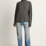 Woman wearing a gray turtleneck sweater and light blue jeans on a white background