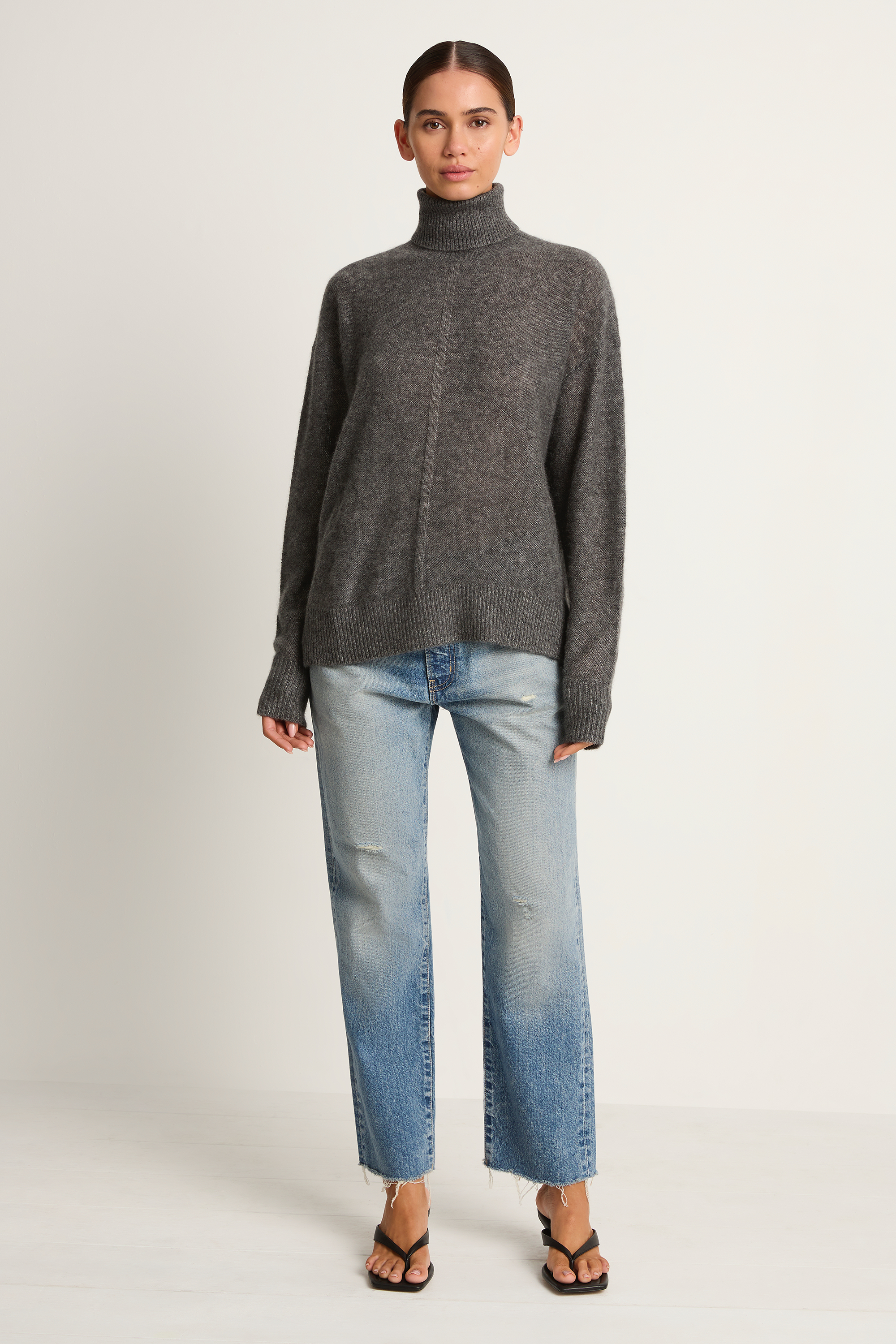 Woman wearing a gray turtleneck sweater and light blue jeans on a white background