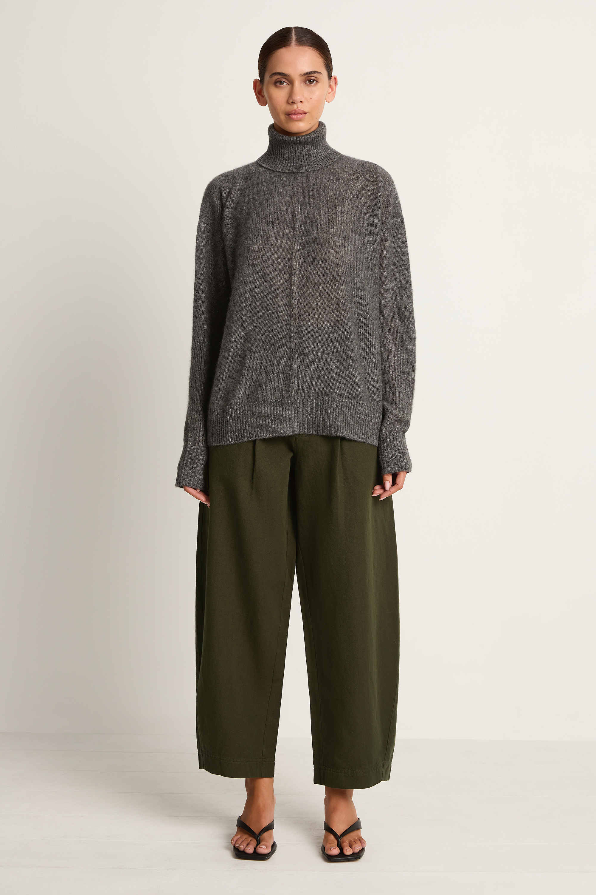 Person wearing a gray turtleneck sweater and olive green pants on a plain background
