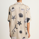 Person wearing a beige shirt with black and gray shell and starfish patterns on a white background