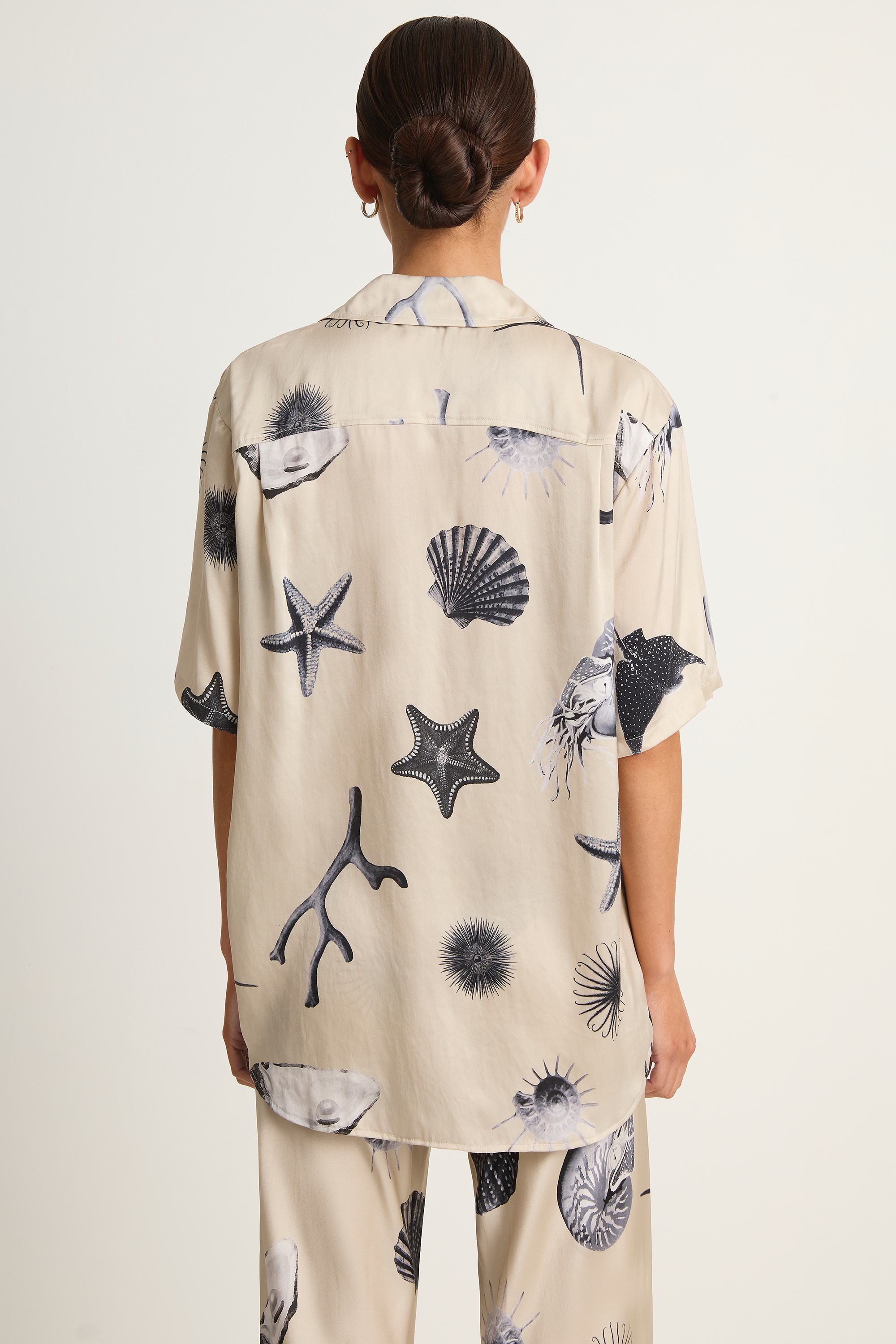 Person wearing a beige shirt with black and gray shell and starfish patterns on a white background