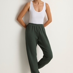 Woman wearing a white tank top and green pants against a plain background
