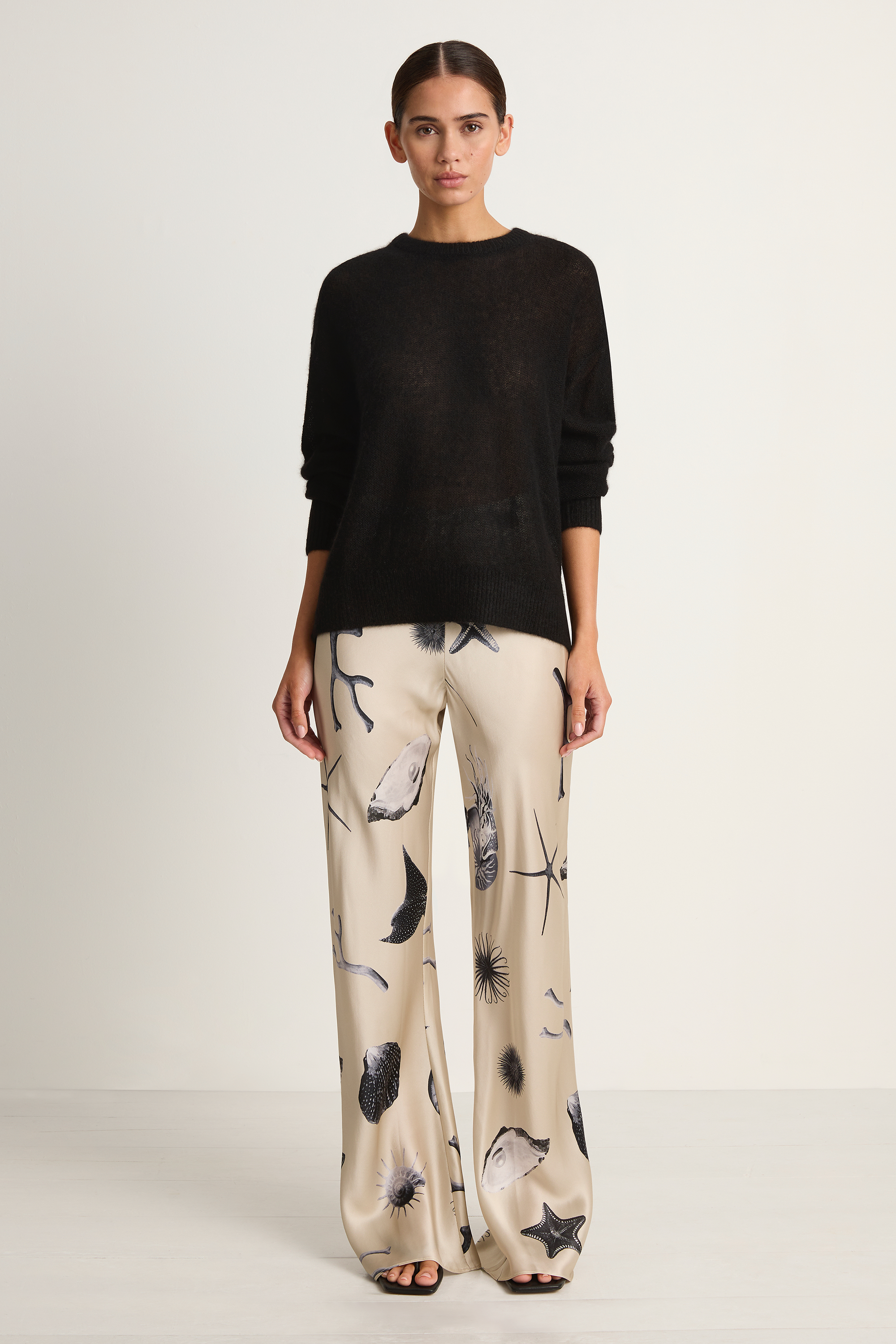 Woman wearing a black sweater and patterned pants on a white background