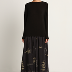 Woman wearing a black long-sleeve top and black skirt with animal concert print on a white background