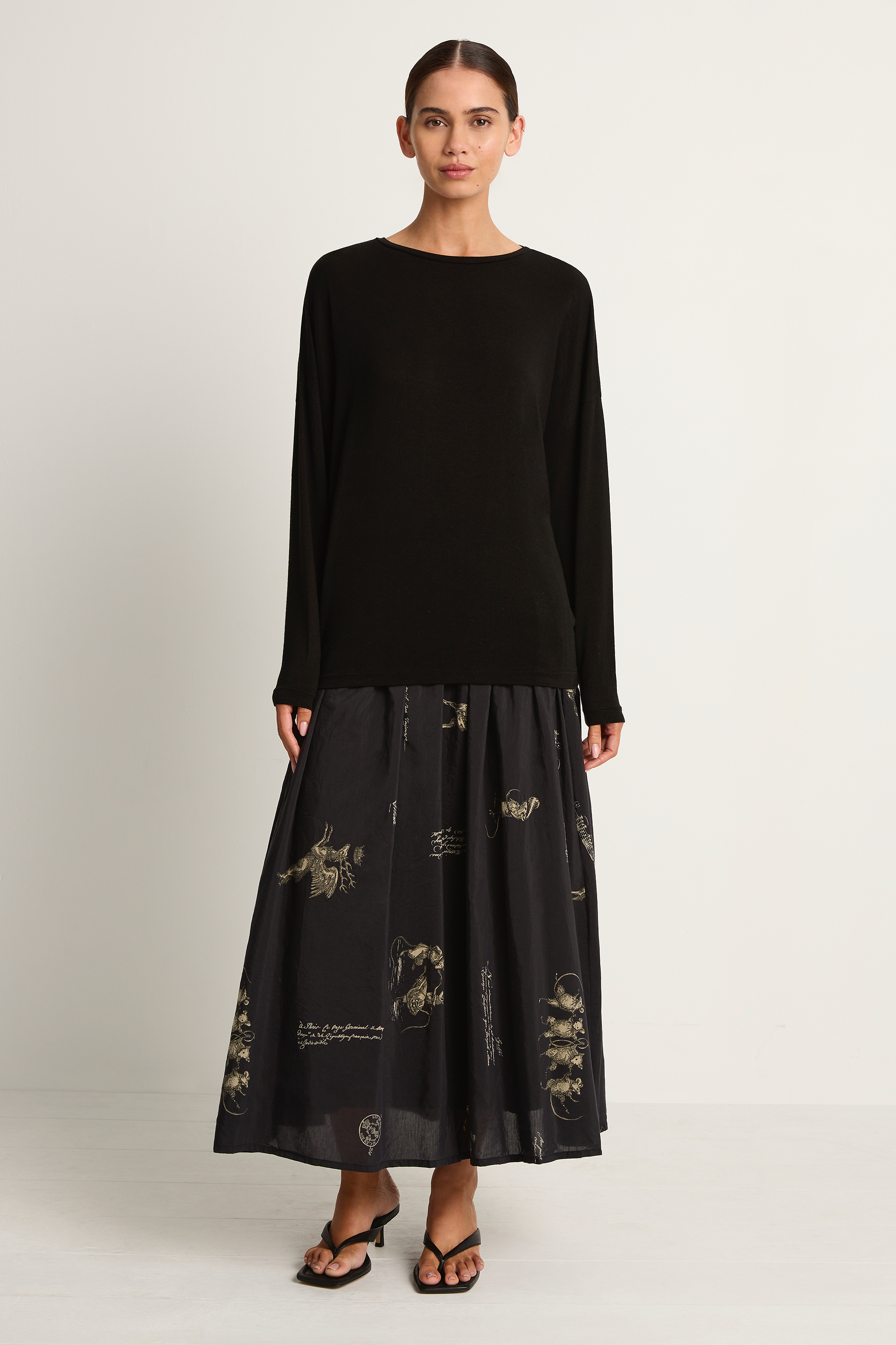 Woman wearing a black long-sleeve top and black skirt with animal concert print on a white background