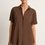 Woman wearing a brown button-up shirt and light blue jeans on a plain background