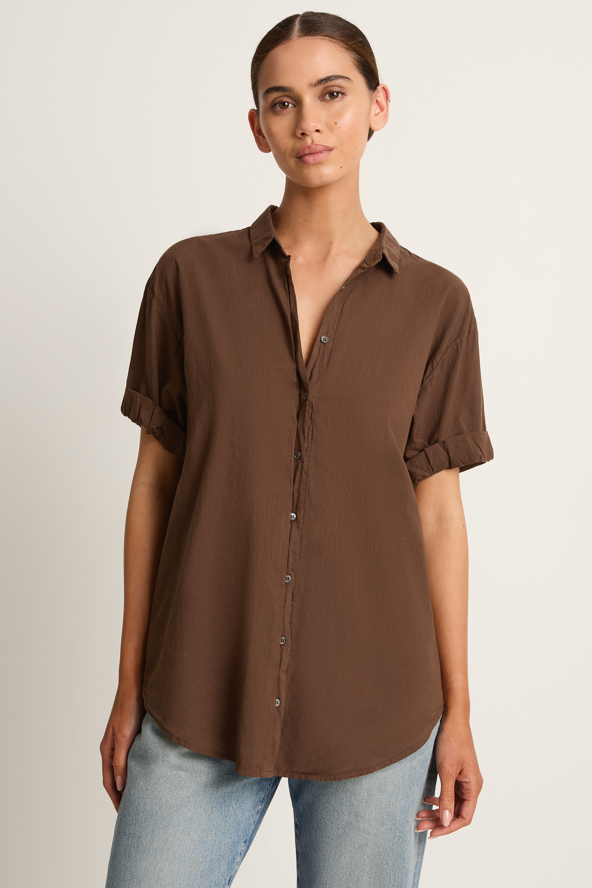 Woman wearing a brown button-up shirt and light blue jeans on a plain background