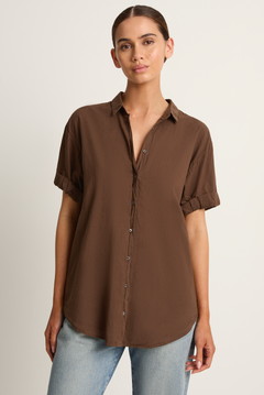 Woman wearing a brown button-up shirt and light blue jeans on a plain background