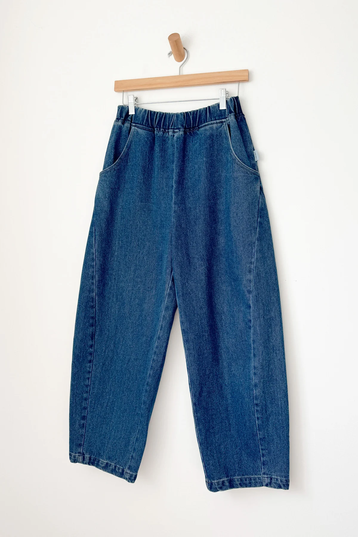 Blue jeans hanging on a wooden hanger against a white background