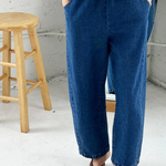Person wearing blue jeans and a white top in a minimalistic setting with a wooden stool.