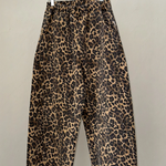 Leopard print pants hanging on a wooden hanger against a plain background