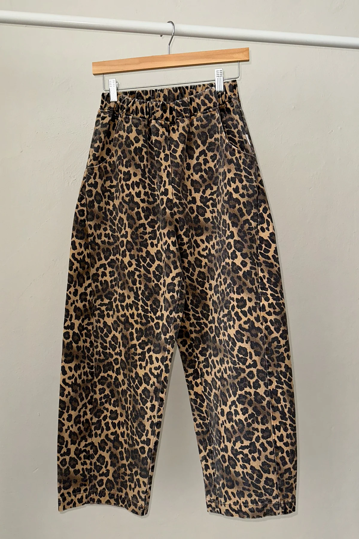 Leopard print pants hanging on a wooden hanger against a plain background
