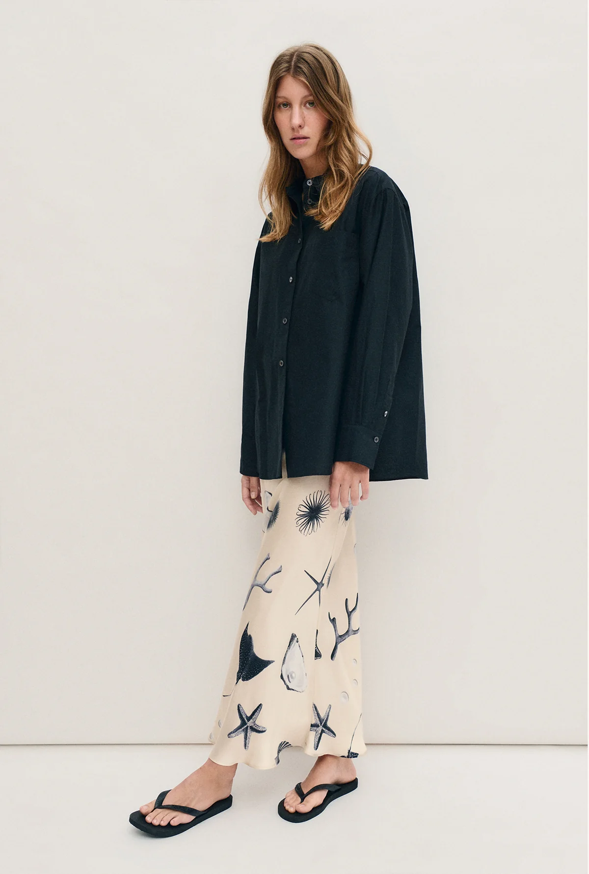Woman wearing a black shirt and patterned pants against a white background