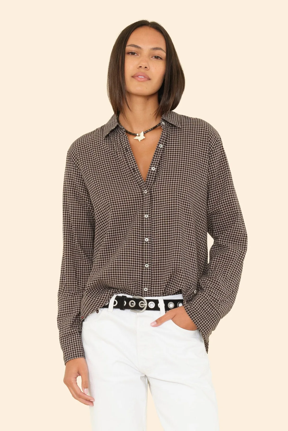 Woman wearing a checkered shirt and white pants on a beige background