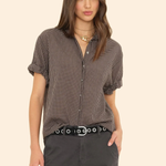 Woman wearing a patterned blouse and dark pants on a beige background